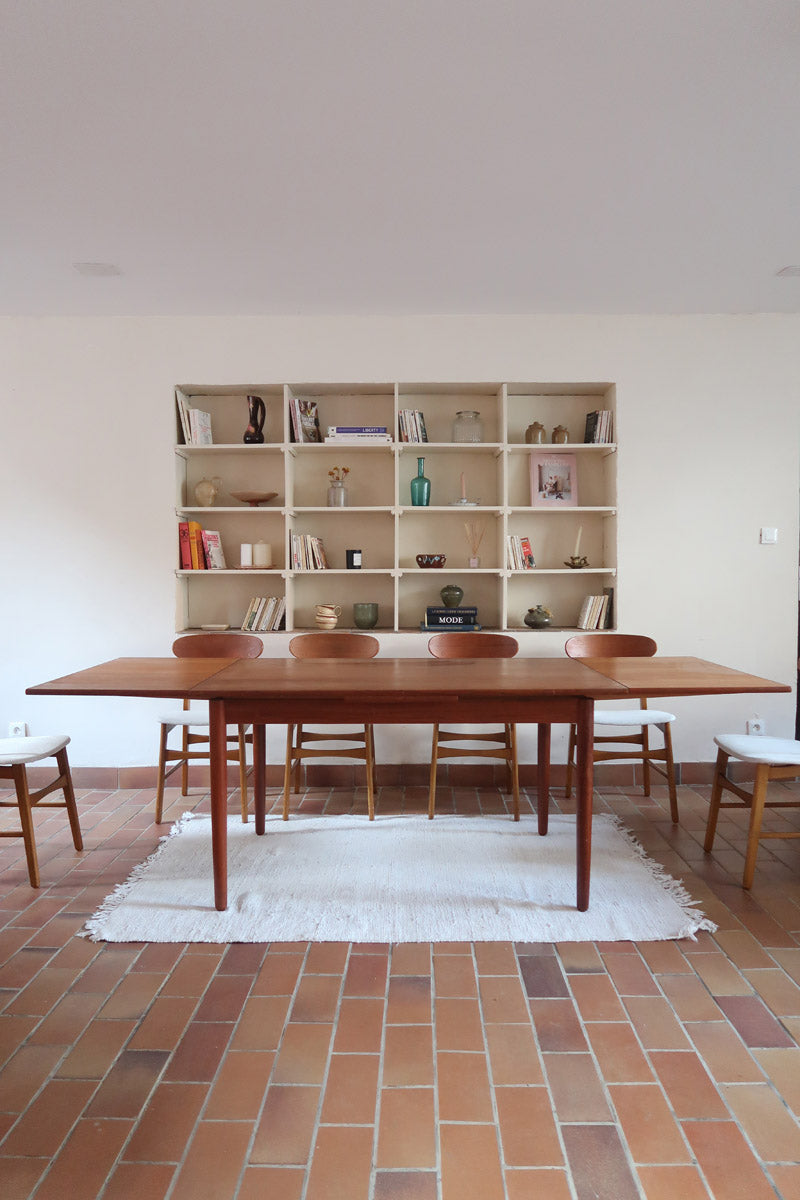 Table à manger scandinave en teck avec deux rallonges intégrées, design années 60, photographiée dans un intérieur lumineux.