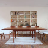 Table à manger scandinave en teck avec deux rallonges intégrées, design années 60, photographiée dans un intérieur lumineux.