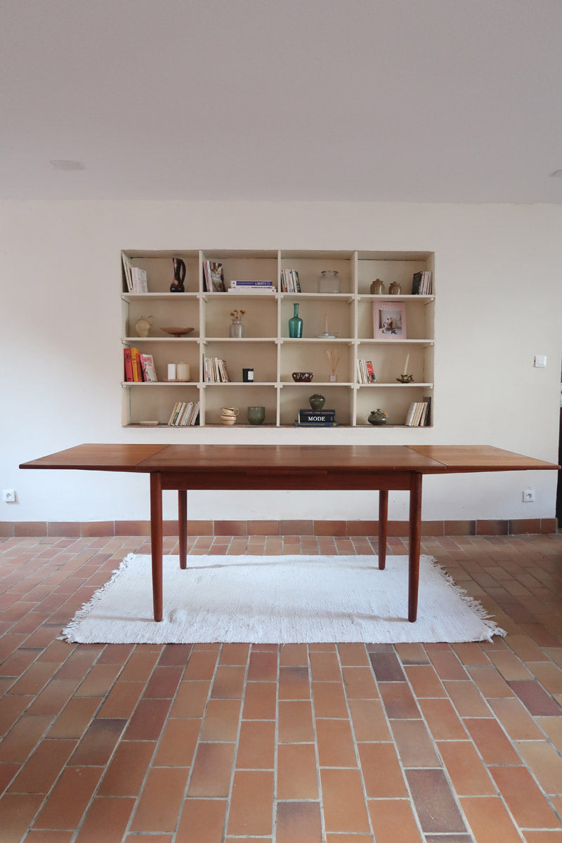 Table à manger scandinave en teck avec deux rallonges intégrées, design années 60, photographiée dans un intérieur lumineux.