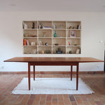 Table à manger scandinave en teck avec deux rallonges intégrées, design années 60, photographiée dans un intérieur lumineux.