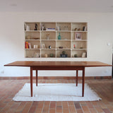 Table à manger scandinave en teck avec deux rallonges intégrées, design années 60, photographiée dans un intérieur lumineux.