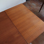 Table à manger scandinave en teck avec deux rallonges intégrées, design années 60, photographiée dans un intérieur lumineux.