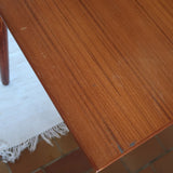 Table à manger scandinave en teck avec deux rallonges intégrées, design années 60, photographiée dans un intérieur lumineux.