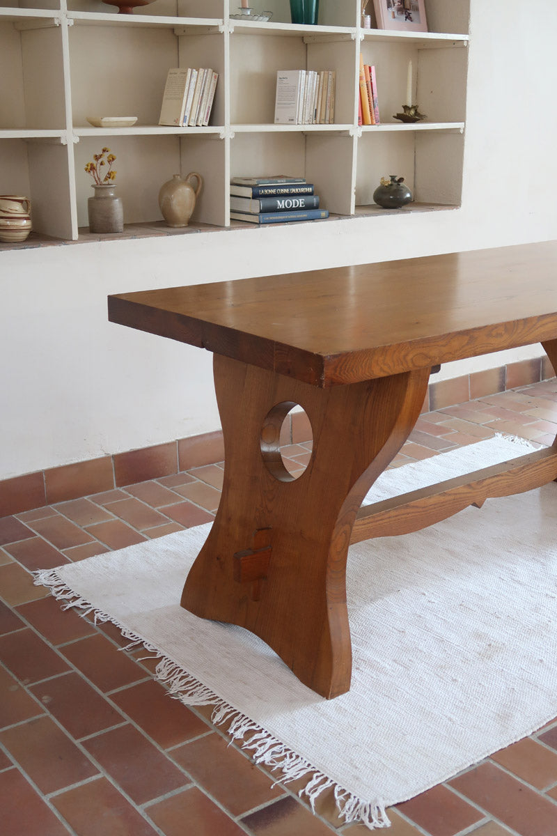 Table à manger vintage en bois massif années 60, plateau épais à chant brut, piétement traîneau sculpté, clé de tenon en croix, travail brutaliste français