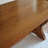 Table à manger vintage en bois massif années 60, plateau épais à chant brut, piétement traîneau sculpté, clé de tenon en croix, travail brutaliste français