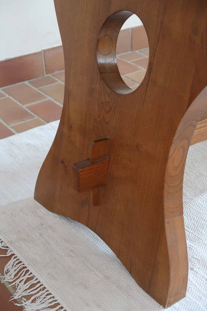 Table à manger vintage en bois massif années 60, plateau épais à chant brut, piétement traîneau sculpté, clé de tenon en croix, travail brutaliste français