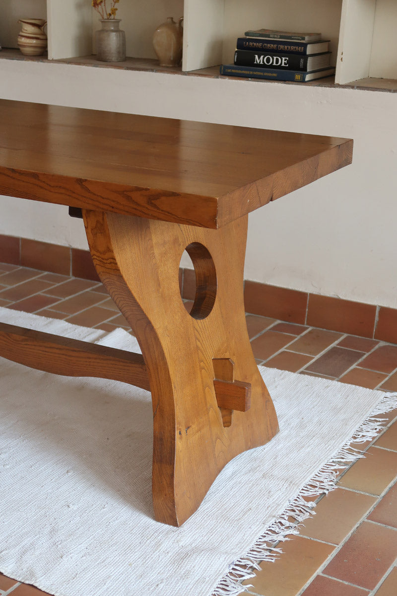 Table à manger vintage en bois massif années 60, plateau épais à chant brut, piétement traîneau sculpté, clé de tenon en croix, travail brutaliste français