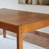 Table à manger extensible en bois massif années 60 avec deux rallonges intégrées sous le plateau.