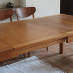 Table à manger extensible en bois massif années 60 avec deux rallonges intégrées sous le plateau.