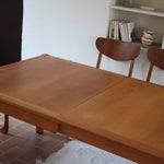 Table à manger extensible en bois massif années 60 avec deux rallonges intégrées sous le plateau.