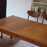Table à manger extensible en bois massif années 60 avec deux rallonges intégrées sous le plateau.