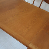 Table à manger extensible en bois massif années 60 avec deux rallonges intégrées sous le plateau.