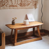 Table basse en bois massif rustique avec plateau épais et piètement trapézoïdal, style brutaliste années 50.