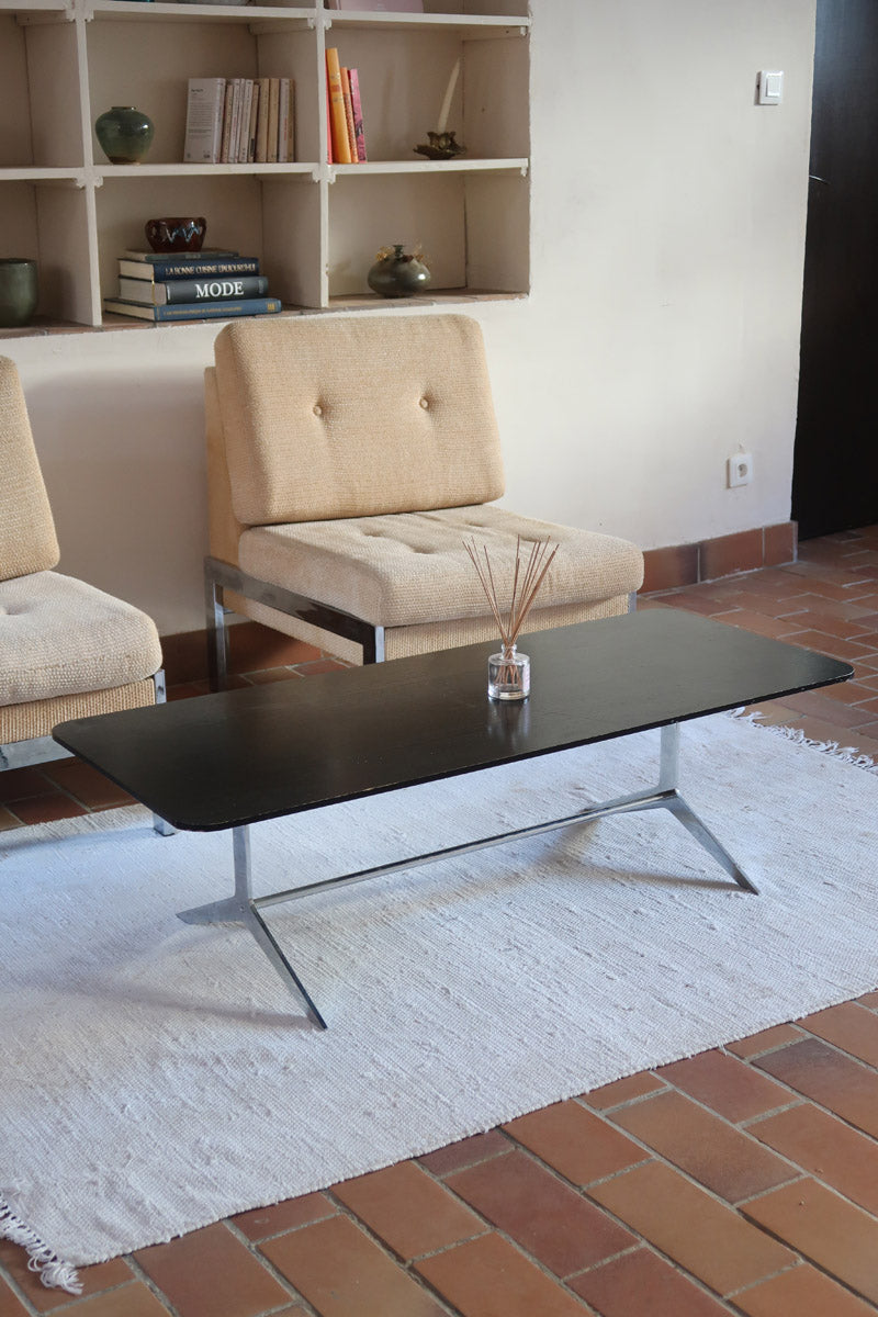 Table basse design années 70 avec plateau noir rectangulaire et piétement en acier brossé en forme de patins.