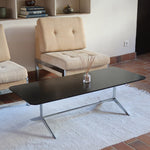 Table basse design années 70 avec plateau noir rectangulaire et piétement en acier brossé en forme de patins.
