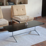 Table basse design années 70 avec plateau noir rectangulaire et piétement en acier brossé en forme de patins.