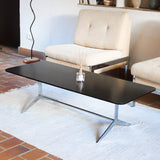 Table basse design années 70 avec plateau noir rectangulaire et piétement en acier brossé en forme de patins.