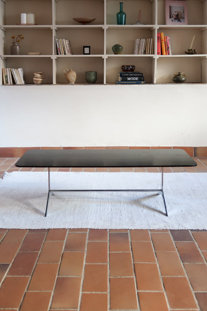 Table basse design années 70 avec plateau noir rectangulaire et piétement en acier brossé en forme de patins.