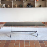 Table basse design années 70 avec plateau noir rectangulaire et piétement en acier brossé en forme de patins.