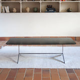 Table basse design années 70 avec plateau noir rectangulaire et piétement en acier brossé en forme de patins.