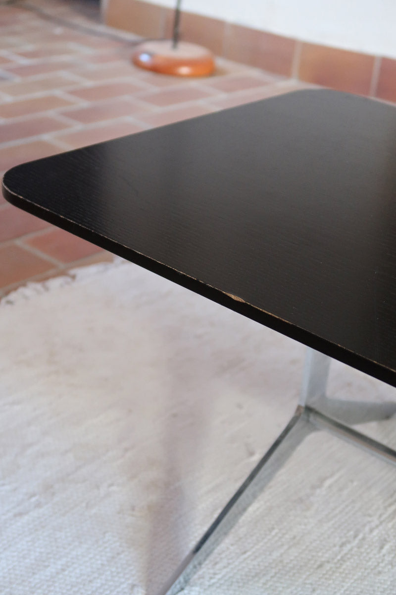 Table basse design années 70 avec plateau noir rectangulaire et piétement en acier brossé en forme de patins.