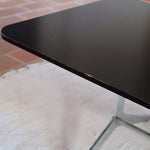 Table basse design années 70 avec plateau noir rectangulaire et piétement en acier brossé en forme de patins.