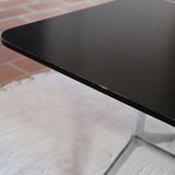 Table basse design années 70 avec plateau noir rectangulaire et piétement en acier brossé en forme de patins.