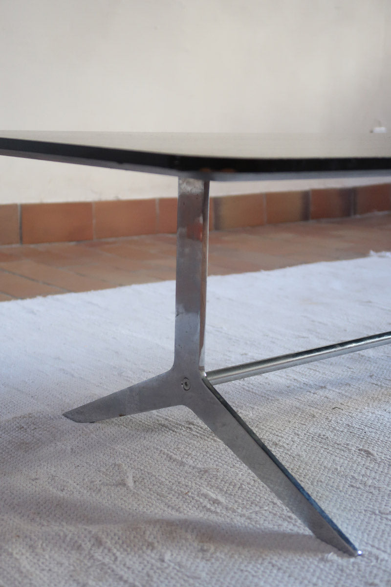 Table basse design années 70 avec plateau noir rectangulaire et piétement en acier brossé en forme de patins.