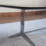 Table basse design années 70 avec plateau noir rectangulaire et piétement en acier brossé en forme de patins.