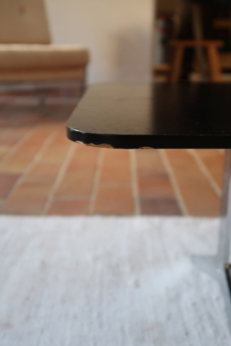 Table basse design années 70 avec plateau noir rectangulaire et piétement en acier brossé en forme de patins.