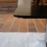 Table basse design années 70 avec plateau noir rectangulaire et piétement en acier brossé en forme de patins.