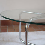 Table basse ronde des années 70 avec plateau en verre et base en tubes chromés en croix.