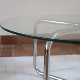 Table basse ronde des années 70 avec plateau en verre et base en tubes chromés en croix.