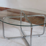 Table basse ronde des années 70 avec plateau en verre et base en tubes chromés en croix.