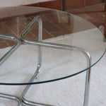 Table basse ronde des années 70 avec plateau en verre et base en tubes chromés en croix.