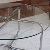 Table basse ronde des années 70 avec plateau en verre et base en tubes chromés en croix.