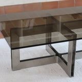 Table basse vintage en verre fumé, années 70, grand plateau rectangulaire à angles arrondis, piétement en inox brossé composé de deux cadres en U réunis par une croix centrale