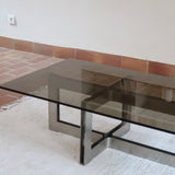 Table basse vintage en verre fumé, années 70, grand plateau rectangulaire à angles arrondis, piétement en inox brossé composé de deux cadres en U réunis par une croix centrale