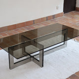 Table basse vintage en verre fumé, années 70, grand plateau rectangulaire à angles arrondis, piétement en inox brossé composé de deux cadres en U réunis par une croix centrale