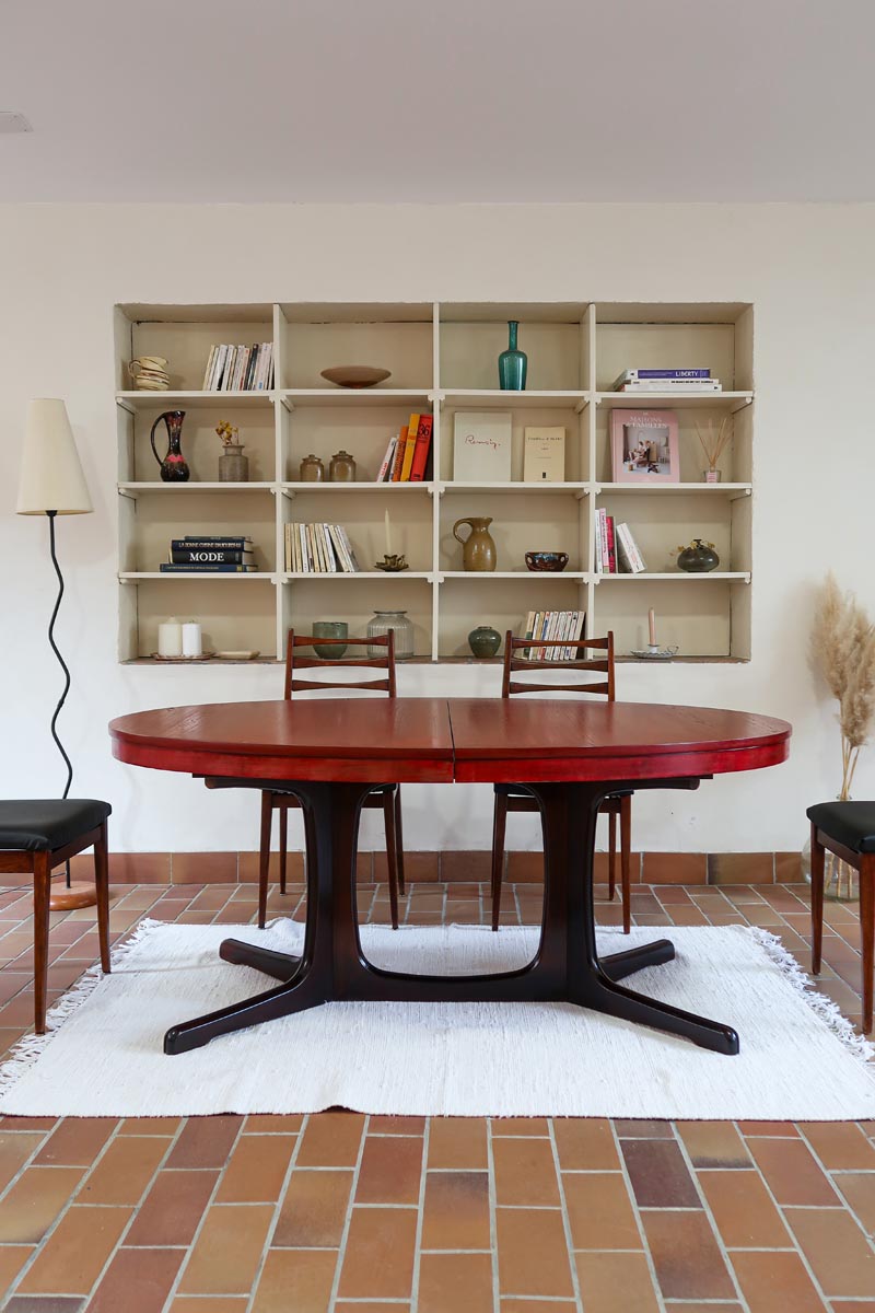 Table à manger ovale en teck avec piètement central sculptural en bois foncé et plateau à teinte rougeâtre, style scandinave vintage, présentée seule et en mise en situation.