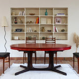 Table à manger ovale en teck avec piètement central sculptural en bois foncé et plateau à teinte rougeâtre, style scandinave vintage, présentée seule et en mise en situation.