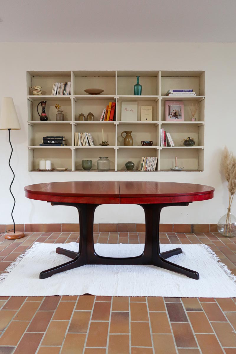 Table à manger ovale en teck avec piètement central sculptural en bois foncé et plateau à teinte rougeâtre, style scandinave vintage, présentée seule et en mise en situation.