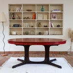 Table à manger ovale en teck avec piètement central sculptural en bois foncé et plateau à teinte rougeâtre, style scandinave vintage, présentée seule et en mise en situation.