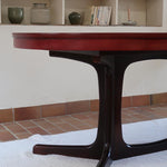 Table à manger ovale en teck avec piètement central sculptural en bois foncé et plateau à teinte rougeâtre, style scandinave vintage, présentée seule et en mise en situation.