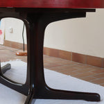 Table à manger ovale en teck avec piètement central sculptural en bois foncé et plateau à teinte rougeâtre, style scandinave vintage, présentée seule et en mise en situation.