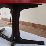 Table à manger ovale en teck avec piètement central sculptural en bois foncé et plateau à teinte rougeâtre, style scandinave vintage, présentée seule et en mise en situation.