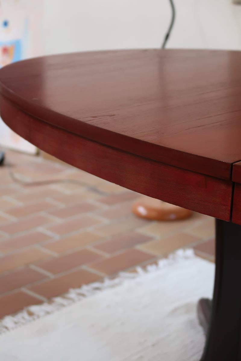 Table à manger ovale en teck avec piètement central sculptural en bois foncé et plateau à teinte rougeâtre, style scandinave vintage, présentée seule et en mise en situation.