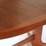 Table à manger ovale en teck avec deux rallonges intégrées, design scandinave des années 60, piètement central en bois.