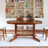 Table à manger ovale en teck avec deux rallonges intégrées, design scandinave des années 60, piètement central en bois.