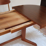 Table à manger ovale en teck avec deux rallonges intégrées, design scandinave des années 60, piètement central en bois.